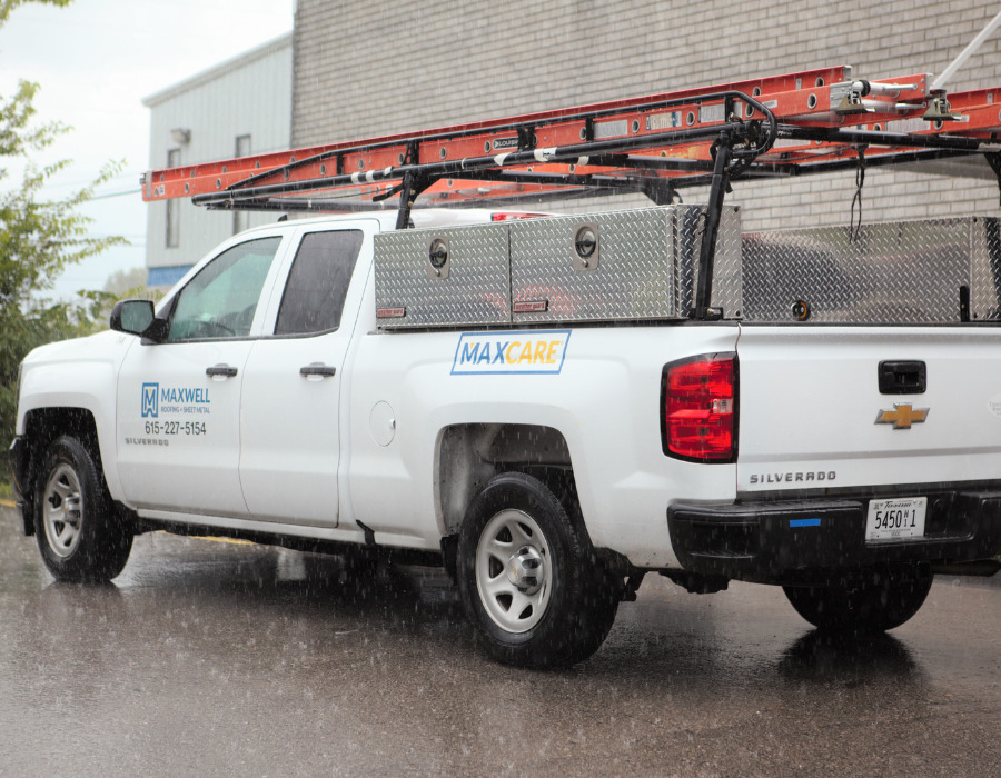 A Maxcare truck parked in the rain with a ladder on the back.